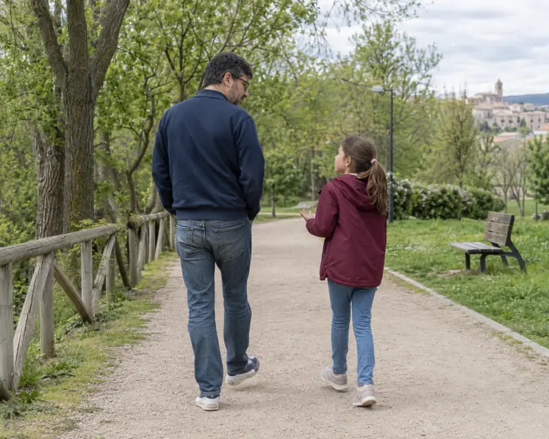 Un padre y su hija conversan mientras pasean por un camino del parque.